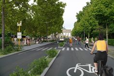 an artist's rendering of people riding bicycles on a street with trees and buildings in the background