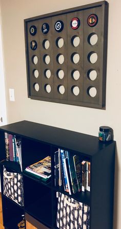 a book shelf with several books and magazines on it in front of a wall mounted game board