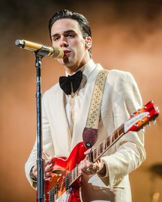 a man in a tuxedo singing into a microphone and playing an electric guitar