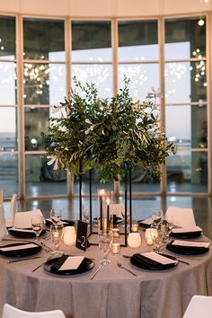 the table is set with black and white place settings, candles, and greenery