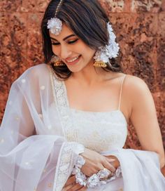 a woman wearing a white sari with flowers in her hair smiling at the camera