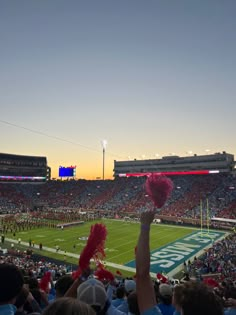 a football stadium filled with lots of people and fans holding up red pom poms