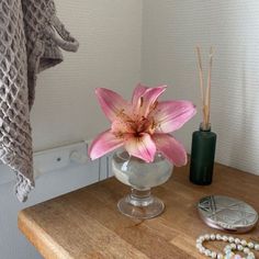 a pink flower sitting in a glass vase on a wooden table next to a towel