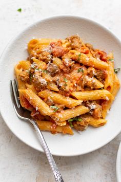 a white bowl filled with pasta and meat on top of a table next to a fork