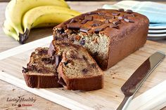 a loaf of chocolate chip banana bread on a cutting board with two bananas in the background