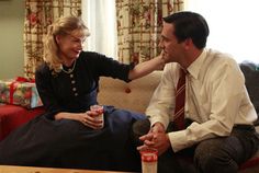 a man and woman are sitting on a couch talking to each other while holding drinks in their hands