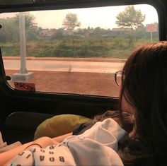 a woman sitting in the back seat of a car looking out at an open road