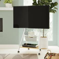 a flat screen tv sitting on top of a white table next to a plant and purse