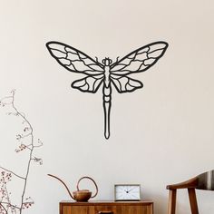 a wall clock with a dragonfly on it next to a table and chair in front of a white wall