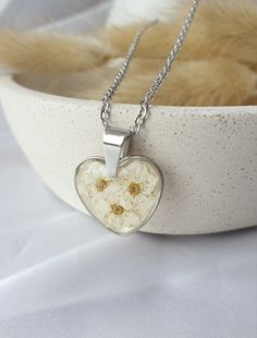 Heart shaped necklace, a harmonious blend of elegance and nature's beauty. Adorned with delicate dry spiraea flowers. The shimmering background adds a touch of radiance to the design, creating a captivating play of light that enhances the intricate detailing. Crafted from high-quality stainless steel, this piece exudes durability and longevity, ensuring it remains a cherished accessory for years to come. White Hypoallergenic Heart-shaped Jewelry, White Stainless Steel Jewelry For Gift, White Stainless Steel Jewelry For Gifts, White Stainless Steel Jewelry Gift, Elegant Heart Pendant Jewelry With Birth Flower Detail, Stainless Steel Heart Pendant Necklace For Mother's Day, Hypoallergenic Jewelry Round Pendant For Gift, White Heart-shaped Hypoallergenic Necklace, Mother's Day Heart Pendant Necklace In Stainless Steel