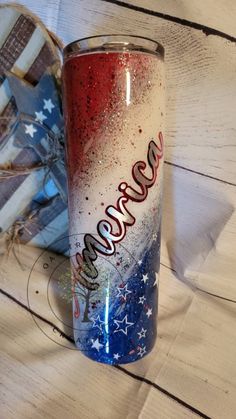 a red, white and blue tumbler sitting on top of a wooden table next to an american flag