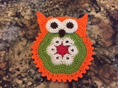 an orange and green crocheted owl sitting on top of a stone slab with a red star in it's center