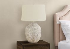 a white lamp sitting on top of a night stand next to a bed with pillows