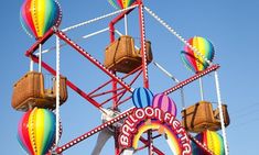 a ferris wheel with several colorful balloons on it's side and a rainbow sign