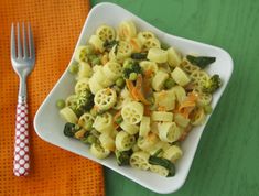 a white bowl filled with pasta and broccoli on top of a green table