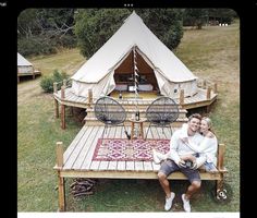 a man and woman sitting on a wooden bench in front of a tent