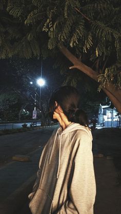 a woman standing under a tree at night with her hand on her face while talking on the phone