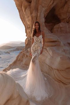 a woman standing in front of some rocks wearing a long dress with flowers on it