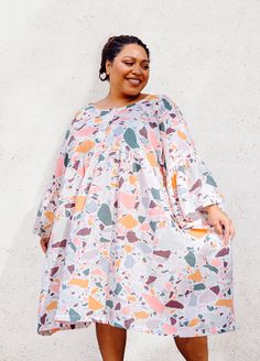 a woman standing in front of a white wall wearing a dress with colorful shapes on it