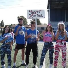 four young people are posing for a photo on the football field, one is holding a sign that says seniors run this