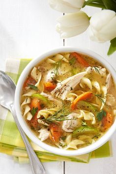 a white bowl filled with chicken noodle soup on top of a green napkin next to flowers