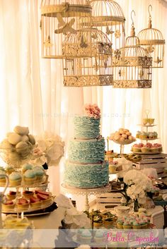 a table topped with lots of cakes and cupcakes covered in frosting next to birdcages