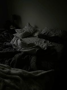 an unmade bed in a dark room with blankets and pillows on top of it