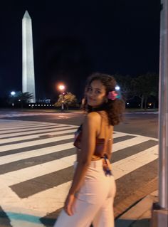 a woman standing in the middle of a crosswalk at night with her back turned to the camera