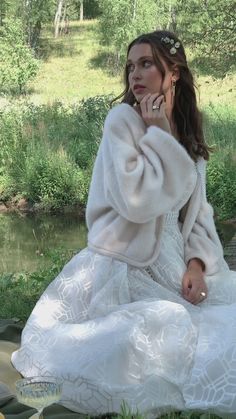 a woman in a white dress sitting next to a river