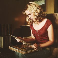 a woman sitting in a chair with a book on her lap and looking at it