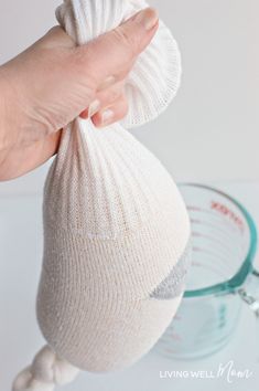 a hand is holding a white knitted object in front of a measuring cup