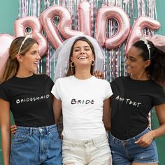 three women standing next to each other in front of pink balloons and the word bride on them