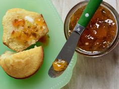 a green plate topped with muffins next to a jar of jelly and a knife