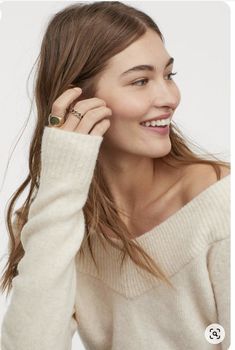 a woman wearing a white sweater holding her hair in one hand and smiling at the camera