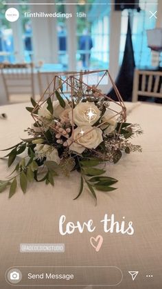 a table topped with a vase filled with flowers and greenery next to a cell phone