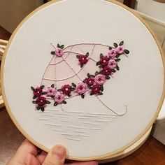 someone is holding up a embroidery project with pink flowers and an umbrella in the middle