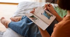 a person sitting on a couch with a notebook and pen in their hand as they look at pictures