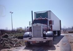 a semi truck is parked on the side of the road in front of an empty field