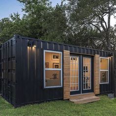 a tiny house made out of shipping containers in the grass with windows and doors open