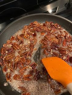 pecans being cooked in a skillet on top of the stove with an orange spatula