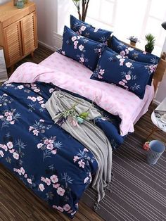 a bed covered in blue and pink sheets with flowers on the comforter next to a window