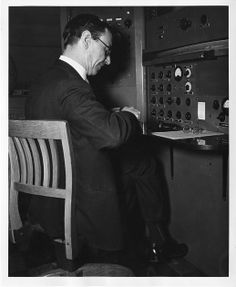 a man sitting in a chair looking at the control panel on an old fashioned machine