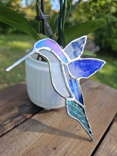 a stained glass hummingbird sitting on top of a wooden table next to a potted plant