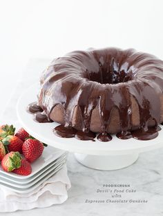 a bundt cake with chocolate icing and strawberries next to it on a plate