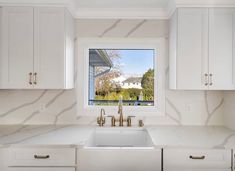 a kitchen with white cabinets and marble counter tops, along with a large window that looks out onto the yard