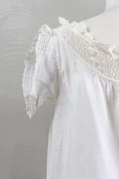 This is a darling antique Edwardian-era white linen shift/chemise. It has a scoop neckline with a lace yoke that is trimmed in a sweet little ruffle. The ruffle also trims the placket that runs down to the waistline and fastens with shell buttons. It has fun little dress protectors style sleeves and are meant to protect the armpit of the dress. On the right side of the placket, there are the original owner's initials A.R.G, in pen. The skirt is simple and hangs loose till past the knees with pretty little pintucks at the hem with a flounce adorned with lace trim. Condition:The shift is in great condition with no flaws to note. It has been professionally hand laundered and is ready to wear.Size:A note on antique shifts. They are meant to be quite loose fitting and the most size restrictive Vintage White Tops With Lace Trim For Daywear, White Linen Top With Broderie Anglaise Detail, White Linen Top With Broderie Anglaise, Vintage White Ruffled Blouse For Daywear, Peasant Tops With Lace Trim For Daywear, Cottagecore Lace Trim Blouse For Daywear, Cottagecore Blouse With Lace Trim For Daywear, Vintage White Blouse With Lace Trim For Daywear, Bohemian Lace Trim Blouse For Daywear