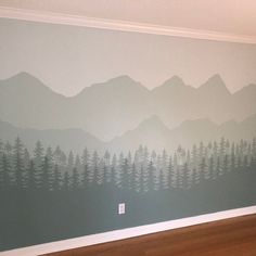 a wall painted with mountains and trees in the middle of a wood floored room