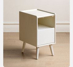 a small white cabinet sitting on top of a hard wood floor next to a wall