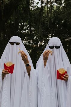 two women dressed in white are holding up mcdonald's fries to their faces and eating them