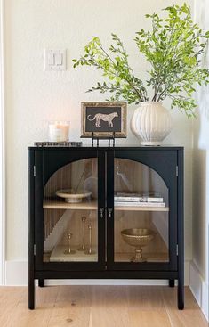 a black cabinet with glass doors and a white vase on the top shelf next to it